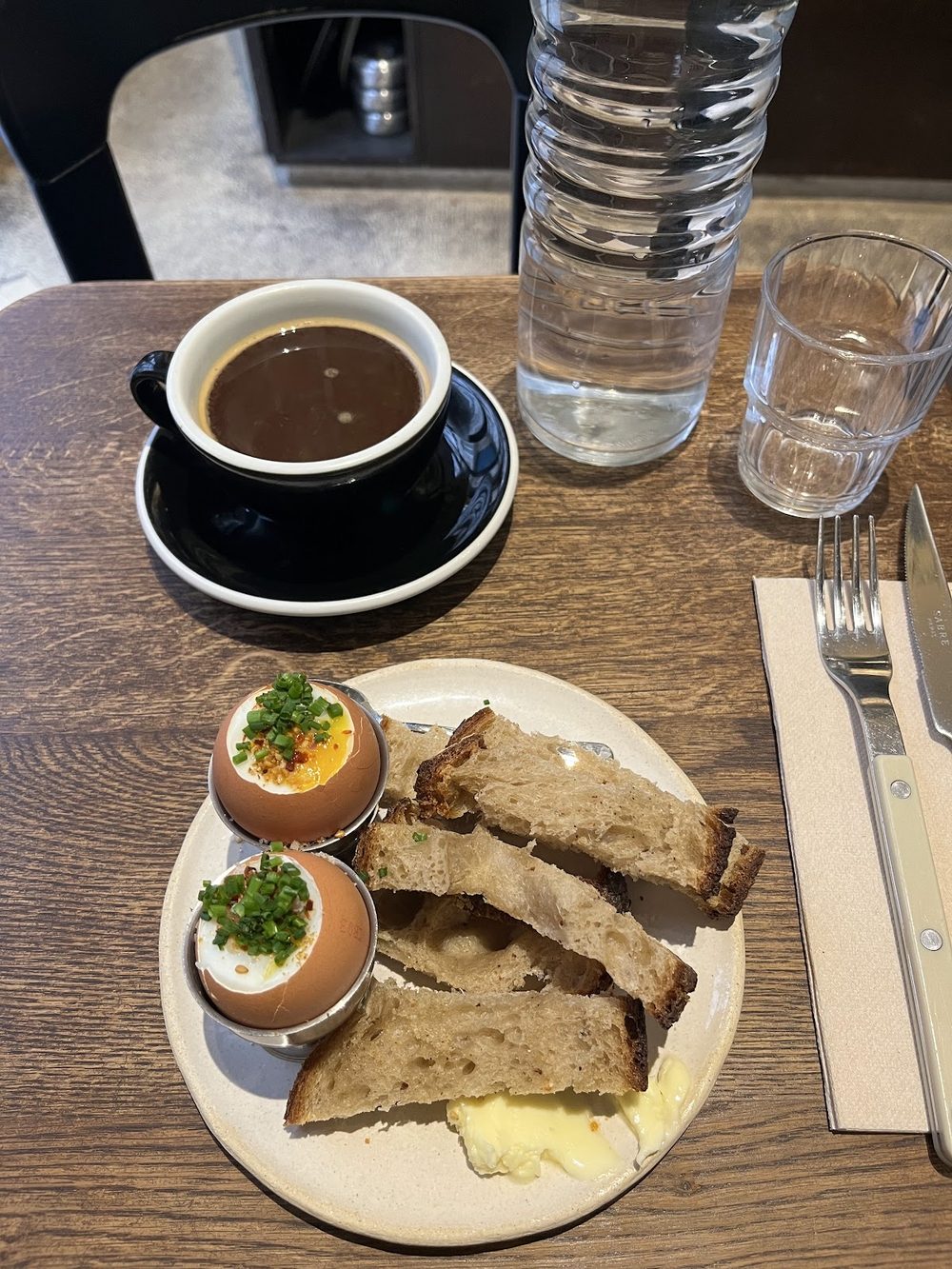 Soft-boiled eggs in their shells with herbs, toasted sourdough and butter, black coffee and a glass of water