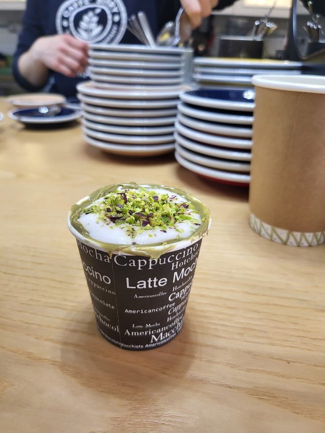 A pistachio yoghurt cup on a cafe table, staff working behind